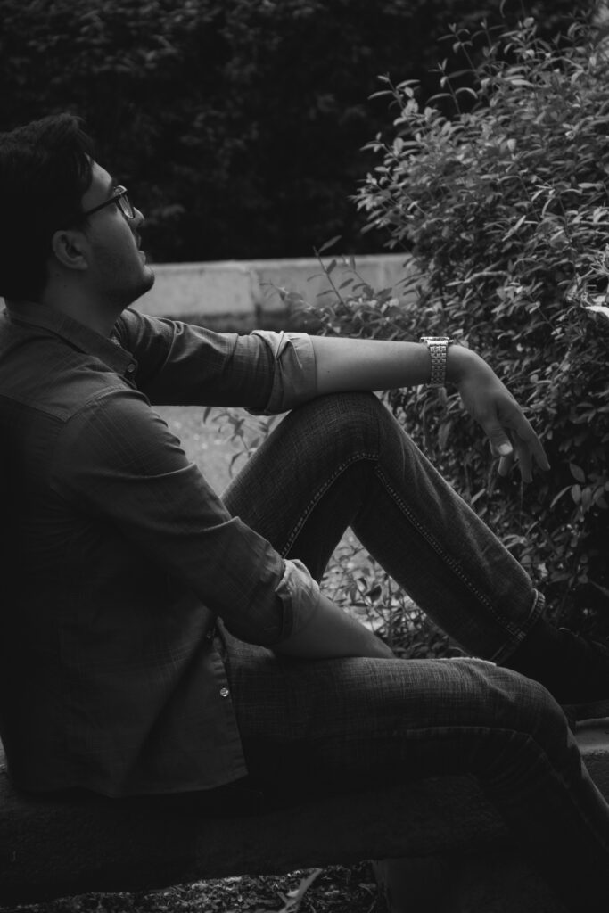 Man sitting outdoors on a bench, looking toward greenery in a quiet reflective moment